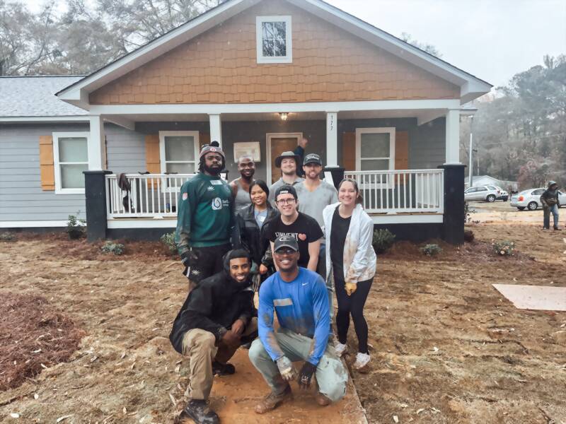 New Acquisitions volunteers in work clothes gathered in front of a Habitat for Humanity home they helped build