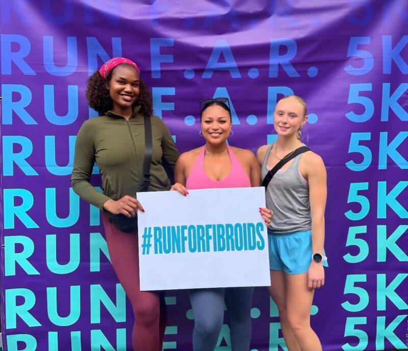 Three New Acquisitions team members holding a Run For Fibroids sign at the Run F.A.R. 5K in Atlanta