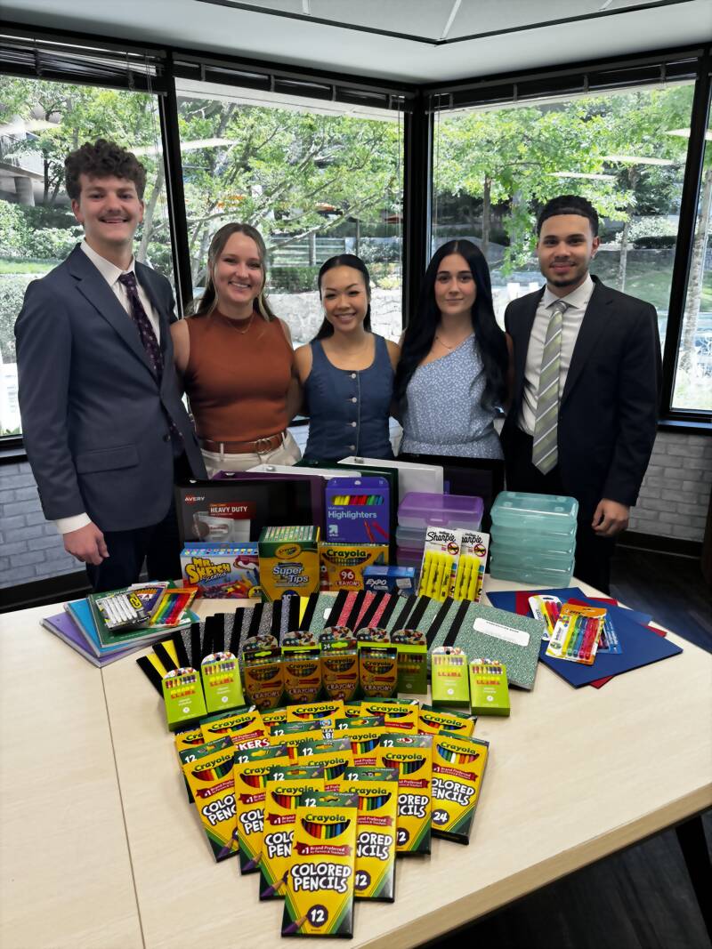 New Acquisitions team members standing behind a table of notebooks, binders, colored pencils and highlighters collected for Baker Elementary in Acworth, Georgia