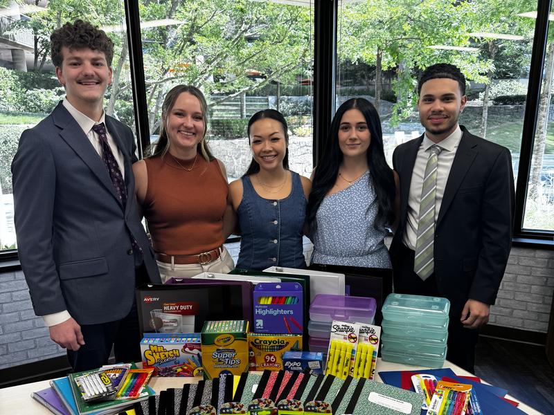 New Acquisitions team members standing behind a table of notebooks, binders, colored pencils and highlighters collected for Baker Elementary in Acworth, Georgia